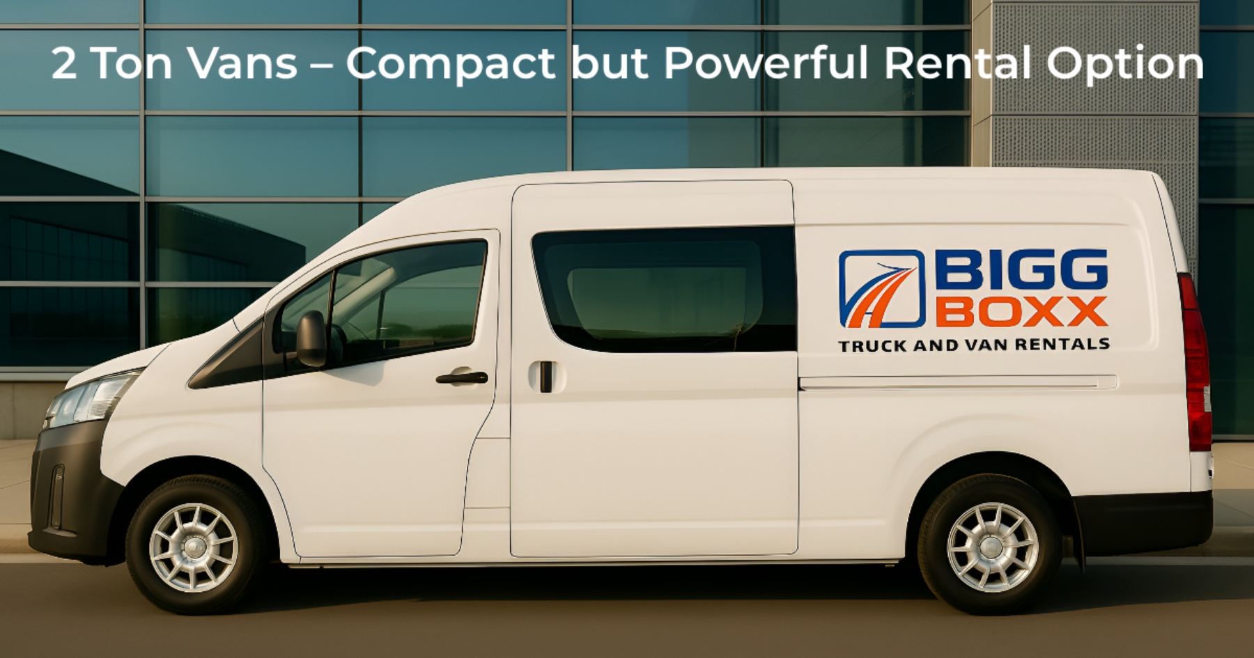 Side view of a white Bigg Boxx 2-ton rental van parked in front of a modern glass-fronted commercial building | 2 Ton Vans – Compact but Powerful Rental Option | Bigg Boxx Rentals