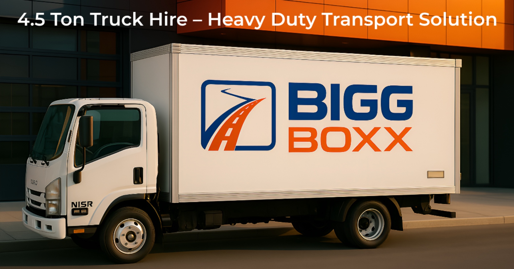 Side view of a white Bigg Boxx 4.5-ton heavy-duty box truck parked in front of a modern orange and grey commercial building | 4.5 Ton Truck Hire – Heavy Duty Transport Solution | Bigg Boxx Rentals