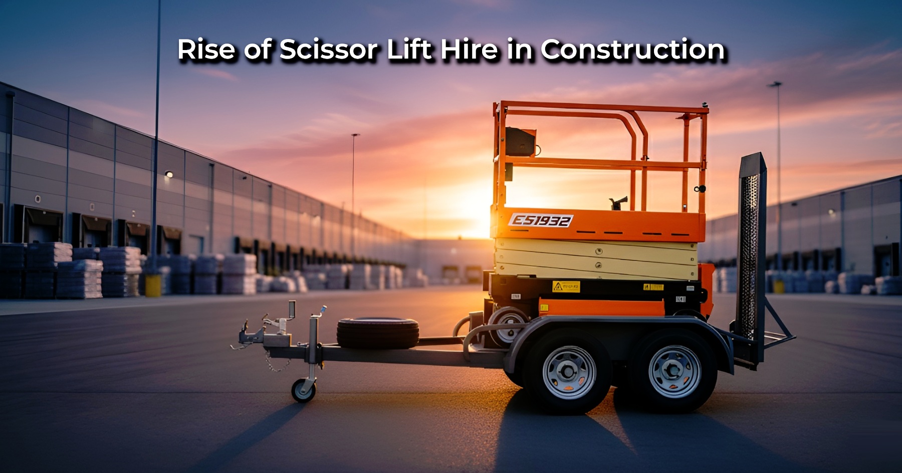 An orange and yellow scissor lift secured on a dual-axle trailer, parked in a large warehouse loading area during a vibrant sunset | Rise of Scissor Lift Hire in Construction | Bigg Boxx Rentals